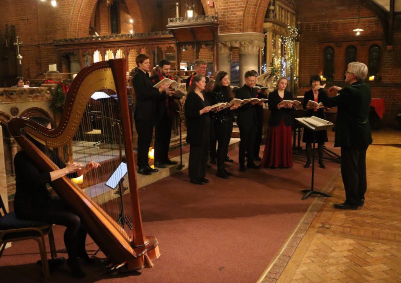 Photo of a choir singing in a church with a harpist playing the harp in the foreground