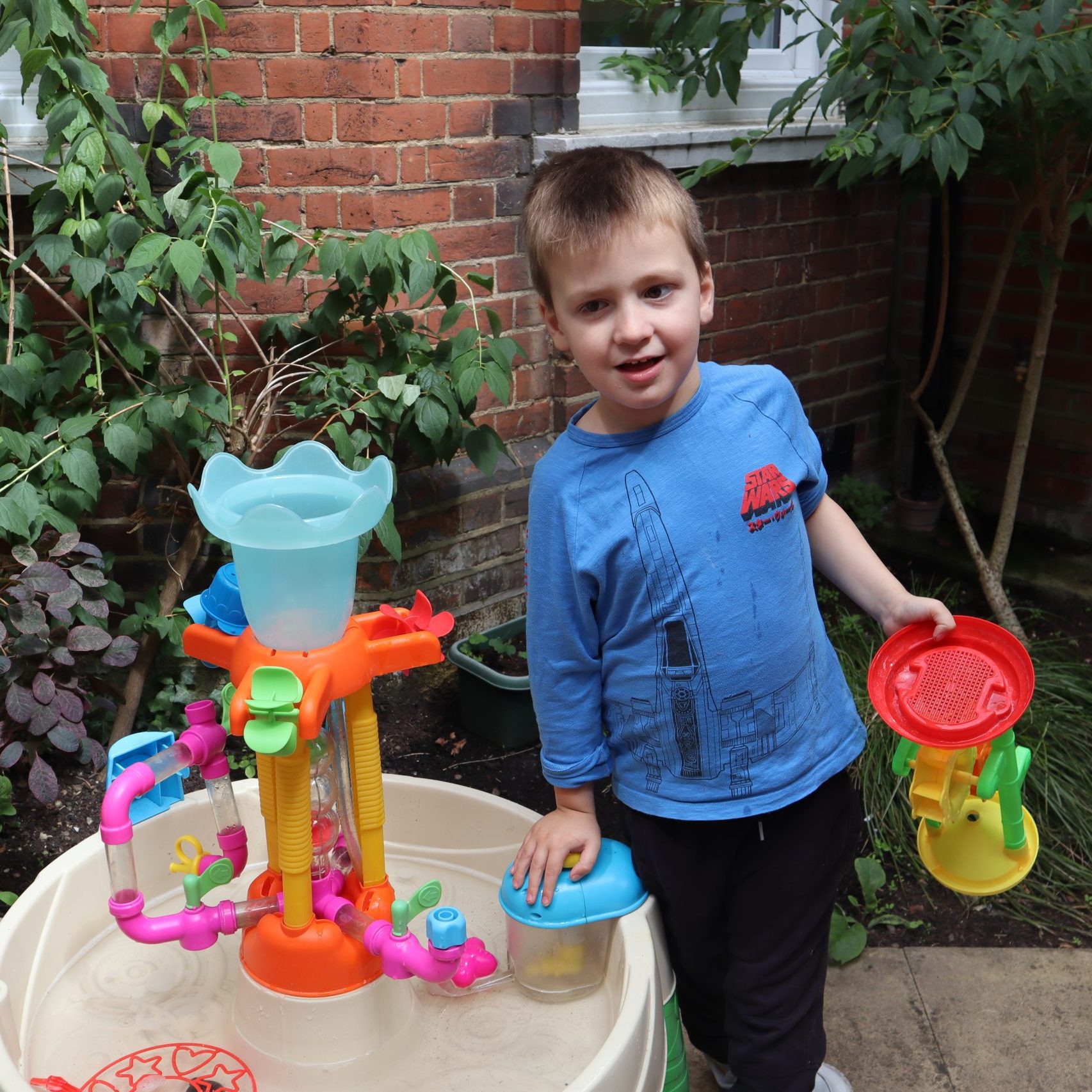 Boy playing outside with water tray and toys